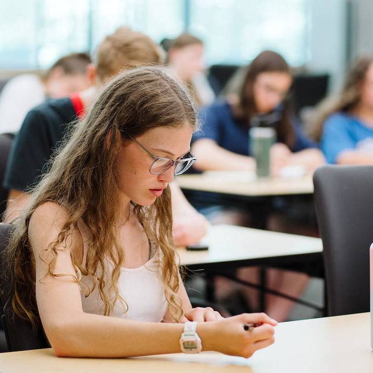 A female high school student takes notes in a classroom.