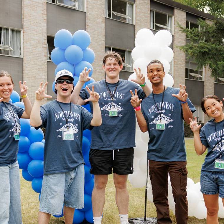 Five current students pose with talons up in front of a large balloon display of the letters NU during Welcome Weekend.
