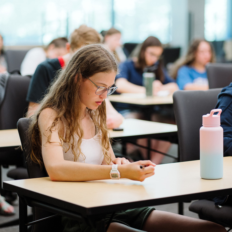 A female high school student takes notes in a classroom.