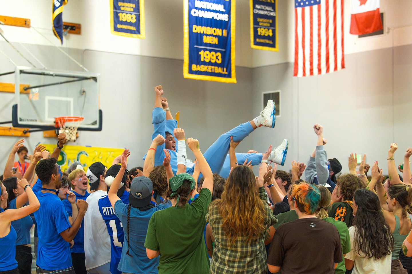 A male students is carried by a crowd of fellow students during a celebration in a gymnasium.