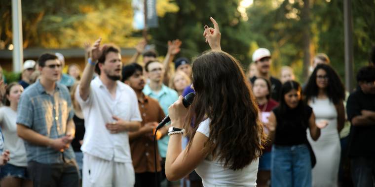 A female student leads a worship service outside on Northwest University's campus.